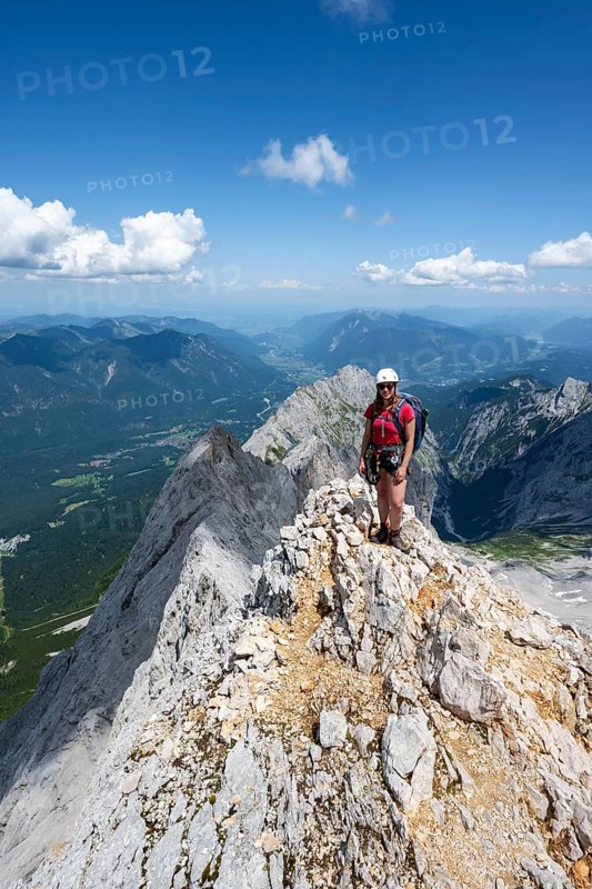 Mountaineer with helmet on a mountain ridge, ascent to the Zugspitze, Zugspitze via ferrata, mountain landscape, view of Eibsee lake and mountain ridge with summit Waxenstein and Riffelspitze, Wetterstein range, Wetterstein range, Bavaria, Germany