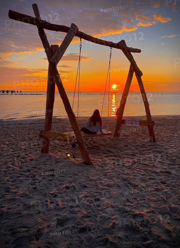 Young girl sitting on a swing on the beach watching sunrise on the island of Rügen, Mecklenburg-Western Pomerania, Germany