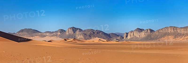 Gentle sand dunes with mountains in the background and a bright blue sky, The landscape of the Sahara in Algeria