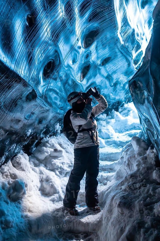 A person is taking a picture in a cave with a backpack on. The cave is filled with ice and snow