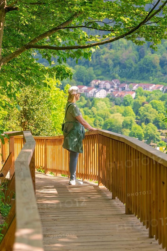 Woman on the wooden path looks at a village in the middle of a spring-like forest landscape, Panorama Holzsteg, Calw, Black Forest, Germany