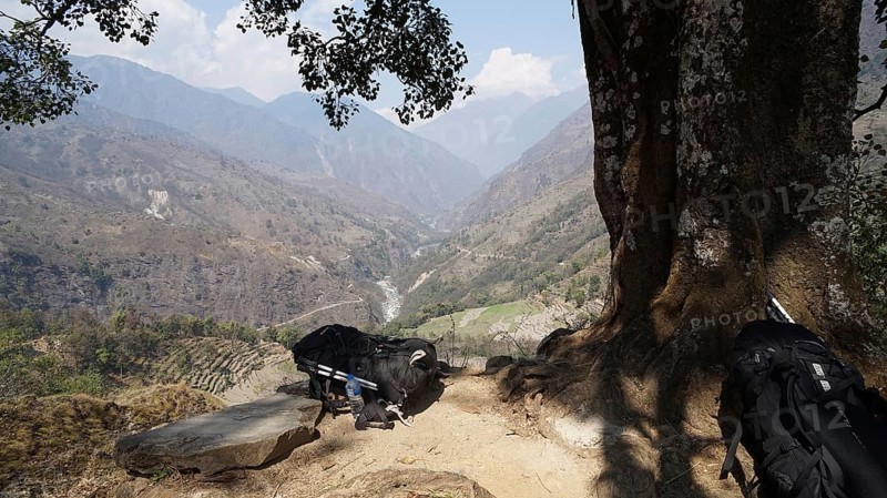 Far reaching view from a vantage point over a river valley and mountain landscape, two large backpacks lying on the ground in front of a tree, trekking at Annapurna Circuit, Nepal