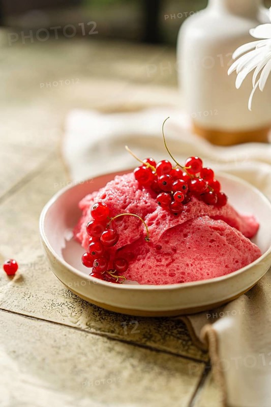 Homemade pink berry mousse garnished with fresh red currants in a ceramic bowl on a tiled table, creating a vibrant food scape