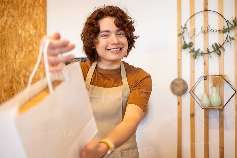 A cheerful shop assistant in an apron hands a paper bag to a customer, creating a warm and welcoming atmosphere in an eco-friendly boutique Wooden decor adds a rustic touch