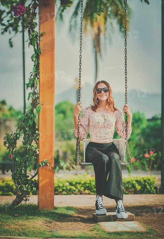 Portrait of a smiling girl sitting on a swing in a nature park. Happy young woman sitting on a swing in a nature park