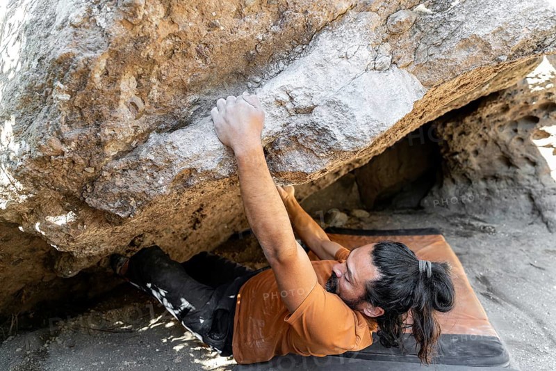 A climber skillfully maneuvers over a challenging boulder in a pristine natural setting, showcasing the thrill and determination of outdoor rock climbing adventures