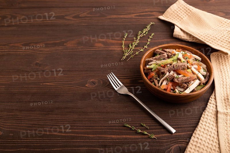 Meat salad with beef and vegetables in wooden bowl on brown wooden background and linen textile. side view, copy space