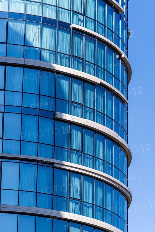 Modern architecture, highlighting a curved building with a vibrant blue glass facade against a clear sky. The structure features elements of concrete, glass, and metal, emphasizing contemporary architectural design and urban aesthetics