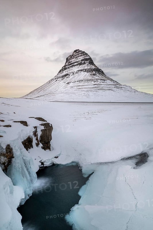 Kirkjufell Mountain, Iceland's iconic landmark, surrounded by a snowy landscape and icy waters, captures the serene beauty of winter in Iceland's natural scenery