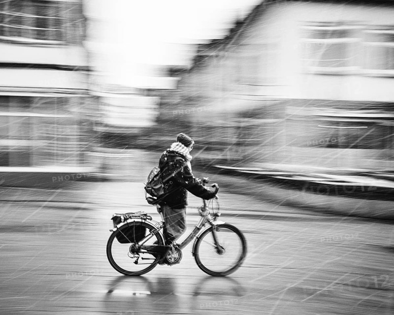 A person on a bicycle rides through a city in bad weather and sleet, rainy day black and white photograph, Baden-Württemberg, Germany