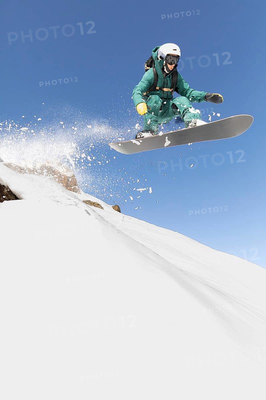 A snowboarder expertly navigates a thrilling freeride descent, capturing the essence of extreme sports in a pristine winter setting. The crisp, clear blue sky frames this exhilarating moment