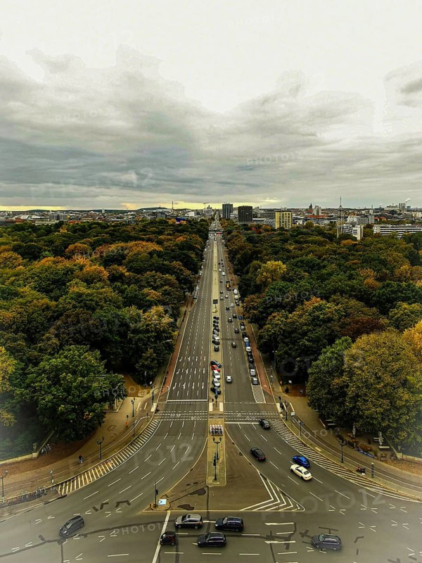 Street in the city surrounded by autumn trees, houses on Hoirzont under cloudy sky, view from Victory Column, Berlin