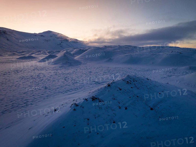 A serene winter twilight spreads over snow-draped hills in Iceland, capturing the tranquil beauty and ethereal glow of the frosty landscape under a pastel sky