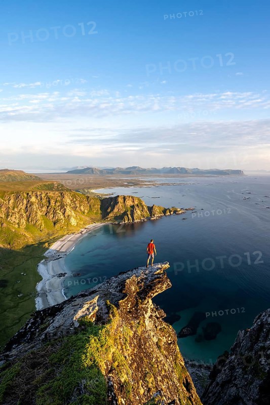 Evening mood, mountaineer standing on a rocky outcrop on the summit of Måtind, view of coastal landscape, Høyvika beach and sea, Måtinden, Andøya island, Vesterålen, Nordland Norway