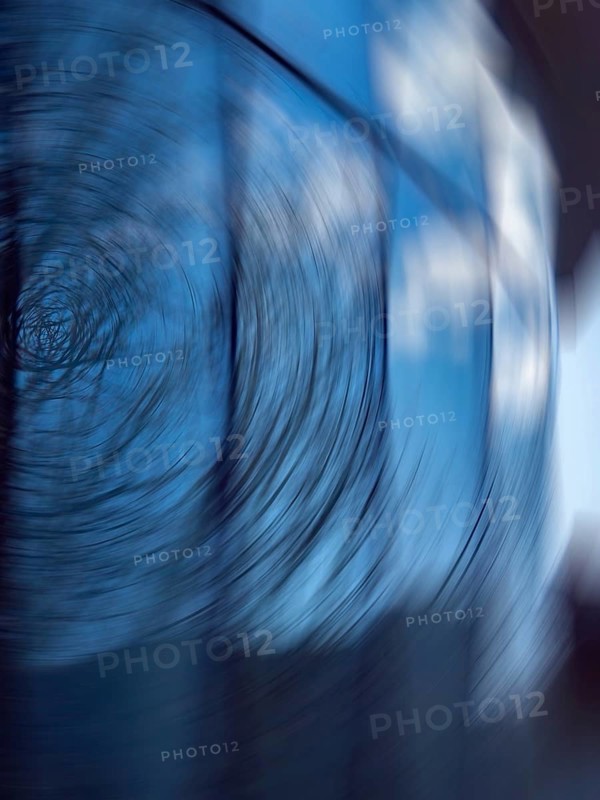 A captivating abstract photograph featuring a swirling motion blur against a blue background. The image includes subtle reflections on glass, creating an intriguing visual effect