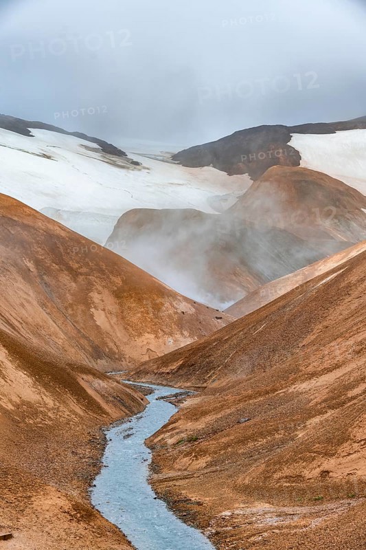 Steaming stream between colourful rhyolite mountains with snowfields, Hveradalir geothermal area, Kerlingarfjöll, Icelandic highlands, Iceland