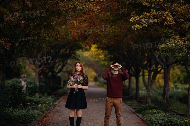 A couple enjoying a beautiful fall day in Quebec, Canada. The woman holds a bouquet of wildflowers, while the man looks through binoculars, surrounded by autumn foliage