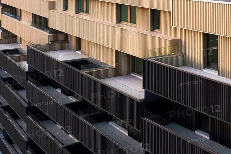 This image showcases a modern apartment building characterized by vibrant colorful portals and a sustainable design aimed at low emissions and high efficiency, epitomizing passive house standards
