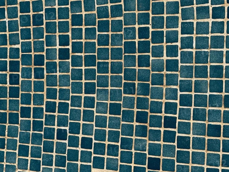 A close-up of a surface adorned with small, blue square tiles arranged in a geometric pattern. The regular grid layout creates a visually appealing modern design