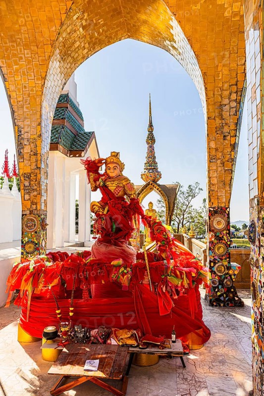 Round arch pavilions decorated with colorful mosaics and glass works of art, including a gilded statue on a red base, Buddhist temple complex Wat Phra That Sorn Kaew, Phetchabun province, Thailand