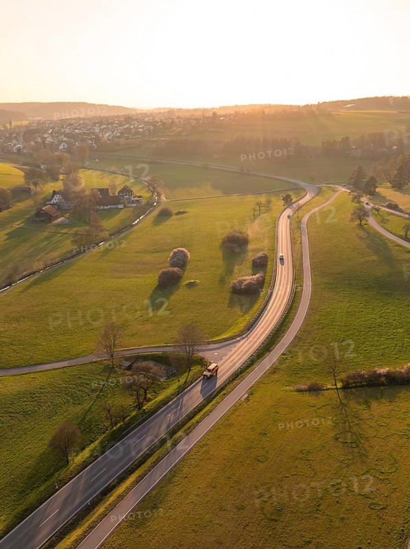 Winding country road through green fields and trees, under a warm sunset sky, Gechingen, district of Calw, Black Forest, Germany
