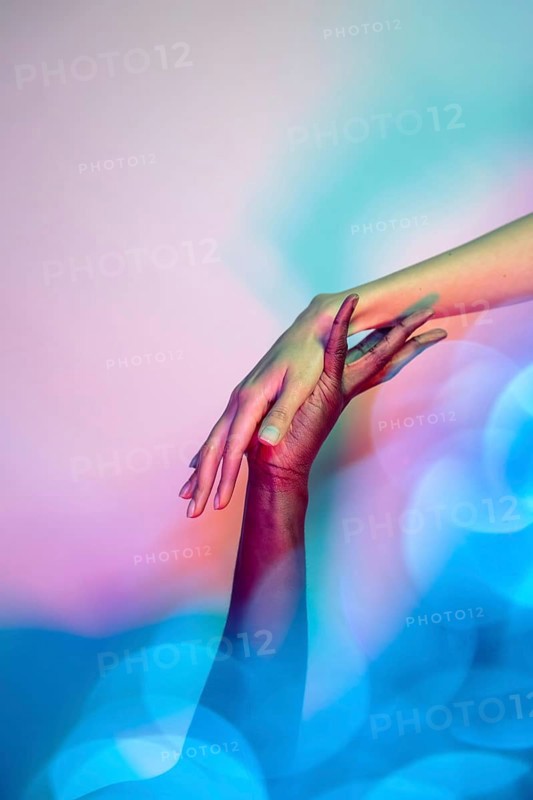 A close-up image of two multiethnic hands reaching towards each other in a gesture of unity and support, set against a vibrant, colorful background symbolizing diversity