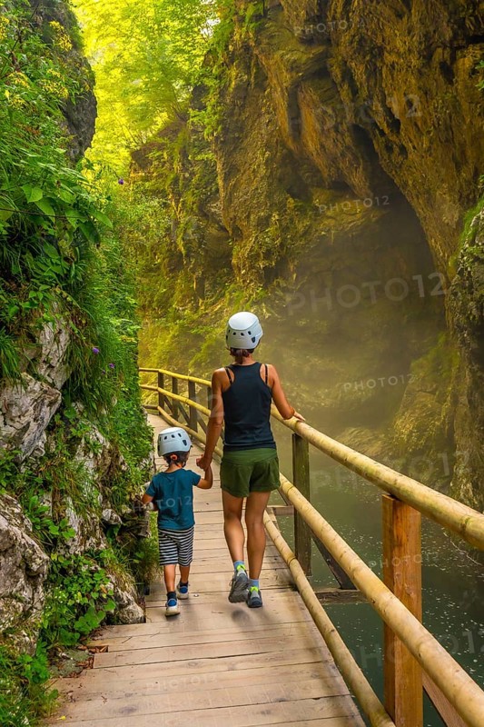 Mother and son wearing helmets are walking on a wooden walkway, exploring the beautiful vintgar gorge near bled, slovenia