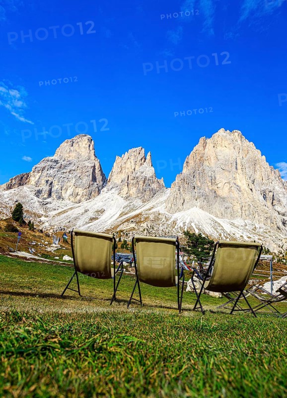 Three camping chairs in a meadow at Passo Sella in front of dramatic mountain peaks under a clear sky