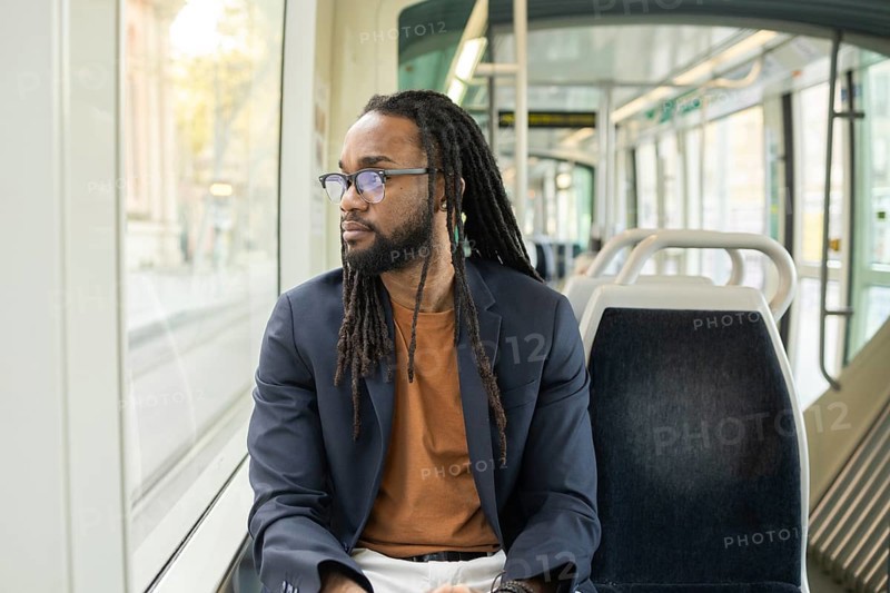A cuban business man sits thoughtfully on a modern tram, gazing out the window. The serene atmosphere of public transport provides a moment of reflection during his commute