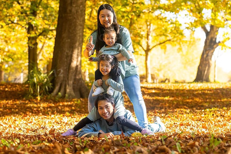 Asian family having fun in an autumn park, with laughter and playful energy. Children enjoying time outdoors, surrounded by fallen leaves and bright sunlight, capturing joy together