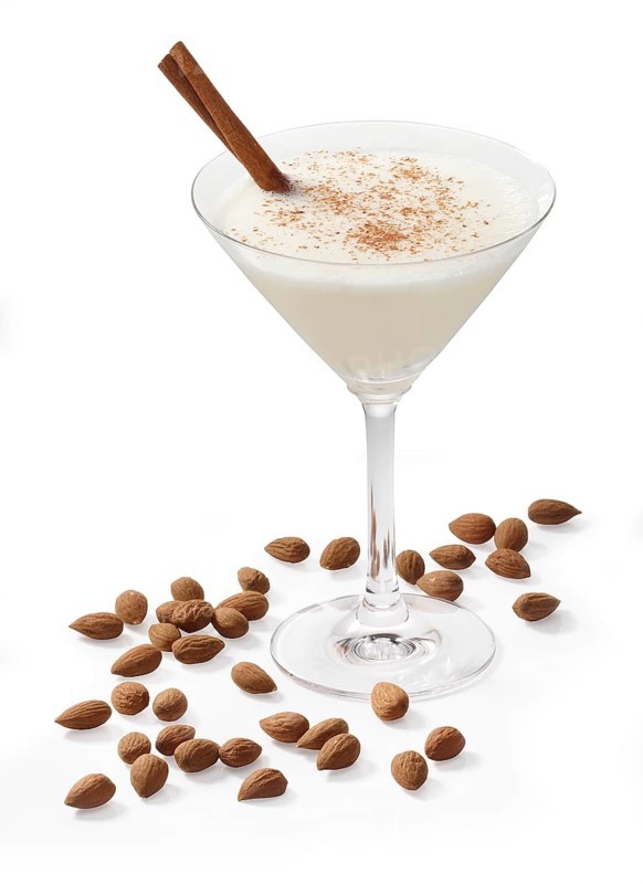 Cocktail in a martini glass in front of a white background, a cinnamon stick and cinnamon powder as garnish, almonds as base decoration, studio shot
