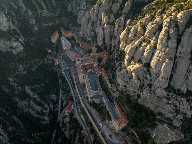 An aerial view of the Montserrat Abbey in Catalonia, Spain, showcases its unique placement amidst rugged mountains, highlighting its architectural beauty and natural surroundings