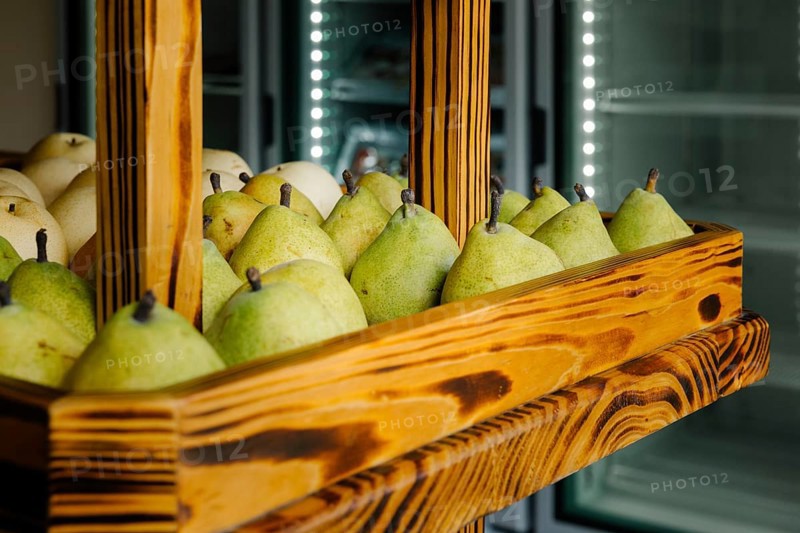 Fresh green pears neatly arranged in a rustic wooden display case at a market in Tulum, Mexico. The vibrant fruit contrasts beautifully with the smooth wooden texture, evoking a sense of local charm and natural abundance