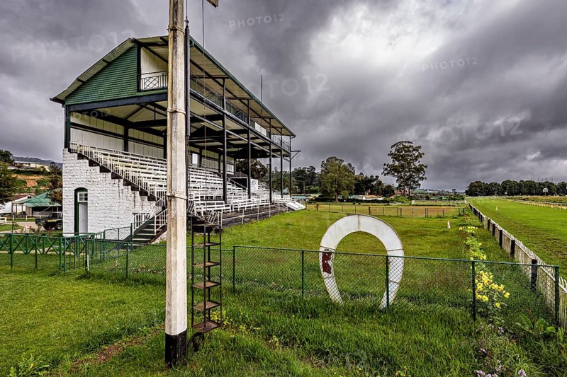 Sports ground with stand and green area under a dramatically cloudy sky, The Nuwara Eliya Sri Lanka Racecourse