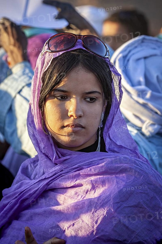 A pensive woman in a purple robe and sunglasses in the evening light, Veiled woman at the Tamanrasett Festival in the Sahara in Algeria