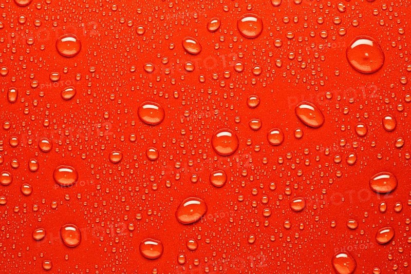 Close up of water droplets on a bright red surface, capturing the texture and varying sizes of the droplets. Ideal for backgrounds, design projects, or abstract art