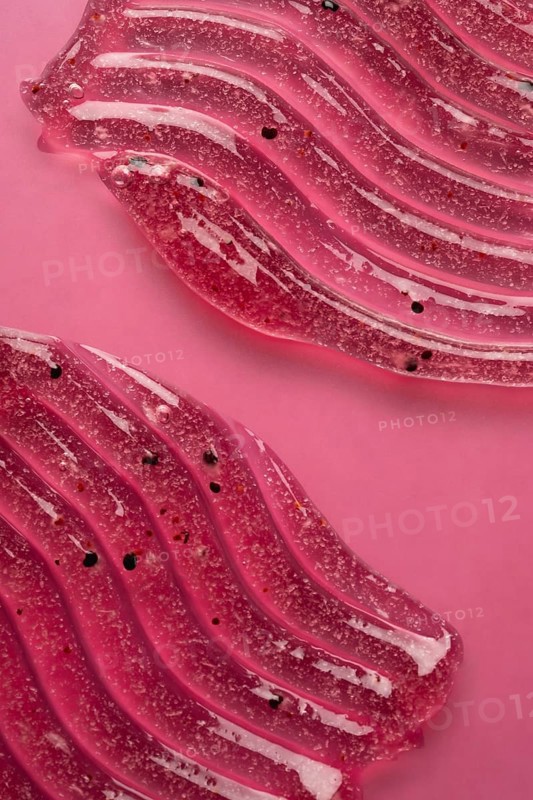 A detailed view of pink scrub and cosmetic gel, elegantly smeared on a pink surface, showcasing the texture and elements within the product