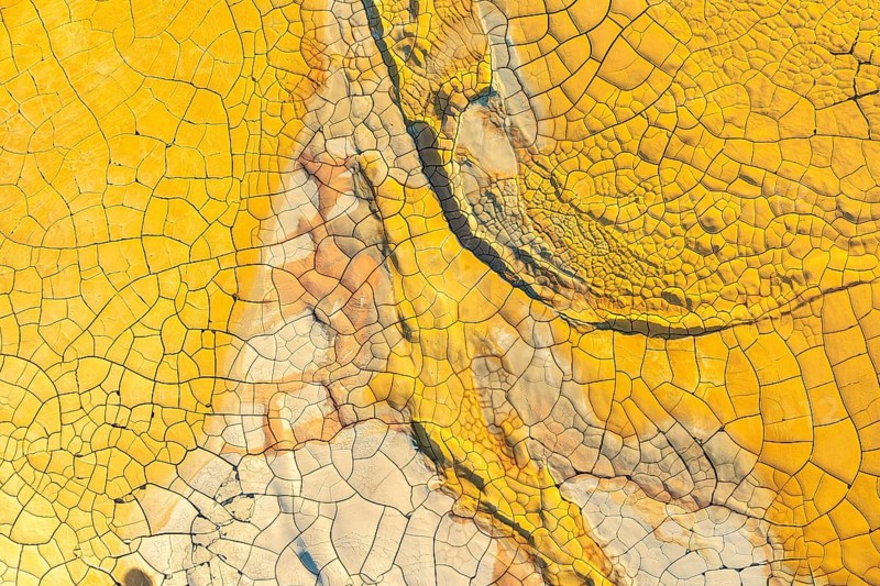 Vibrant, high-resolution image showcasing the intricate patterns and deep cracks of dried, golden mud. Ideal for backdrop or texture use