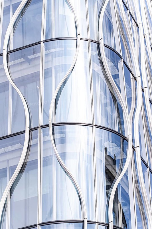 Stunning modern architecture showcasing a sleek, curved glass facade. The reflective surfaces and elegant lines create a dynamic and sophisticated urban visual