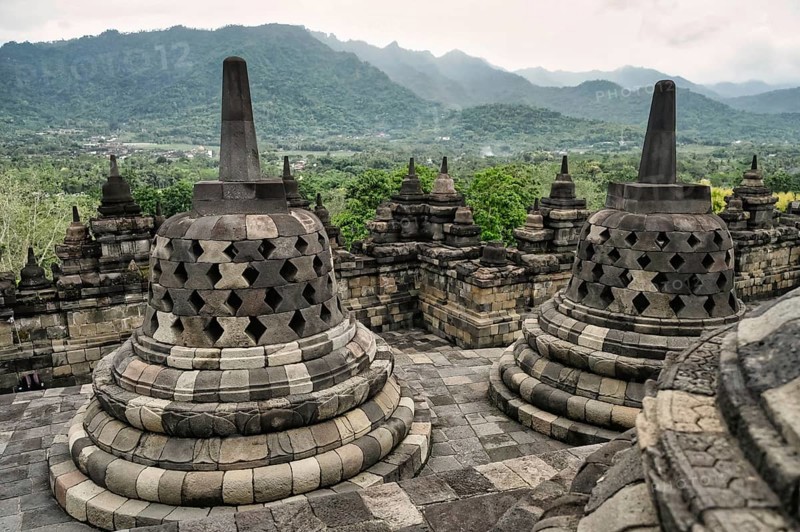 Majestic view of the Borobudur Temple's ancient stone stupas, with vibrant green mountains and lush scenery in the background, highlighting Indonesia's cultural heritage