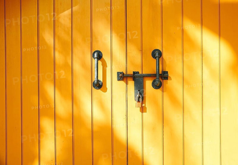 Yellow wooden door in California, USA, featuring strong metal handles and a padlock. Sunlight casts soft patterns, creating a vibrant and secure atmosphere