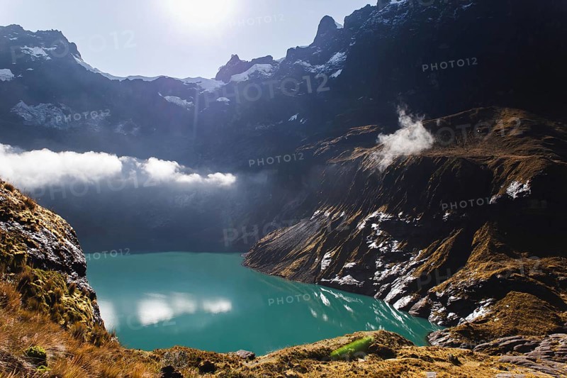 A stunning turquoise crater lake at El Altar volcano, Ecuador, surrounded by rugged peaks, golden sunlight, and misty clouds, creating a dramatic and serene Andean landscape