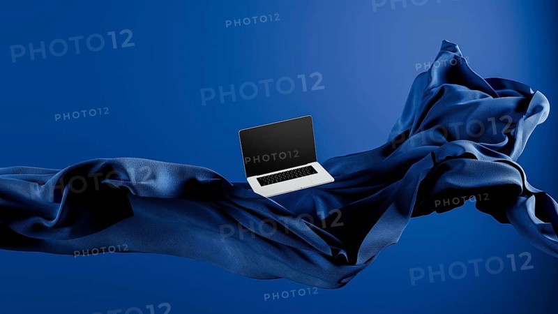 A sleek laptop is placed atop smooth fabric, showcasing its lightweight design against a rich blue backdrop