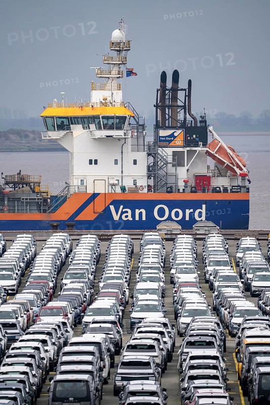 Parking space for import vehicles, hundreds of Hyundai Ioniq, electric cars, waiting for onward transport, behind them, on the Weser, the dredger, the hopper dredger, suction dredger, Vox Ariane, which holds the tug to a certain depth, at the EUROGATE container terminal in the overseas port of Bremerhaven, Lower Saxony, Germany