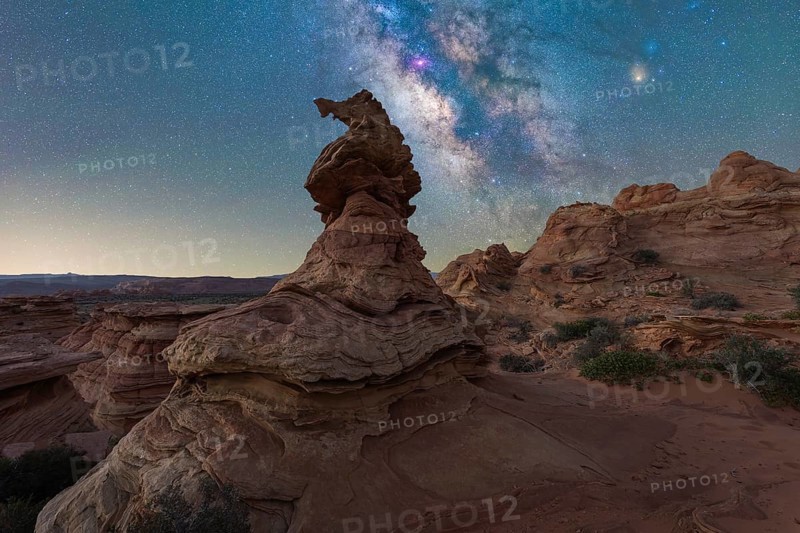 A breathtaking view of a starlit sky over unique rock formations in a desert landscape in Coyote Buttes, Arizona. The Milky Way vibrant colors contrast with rugged terrain, creating a serene scene