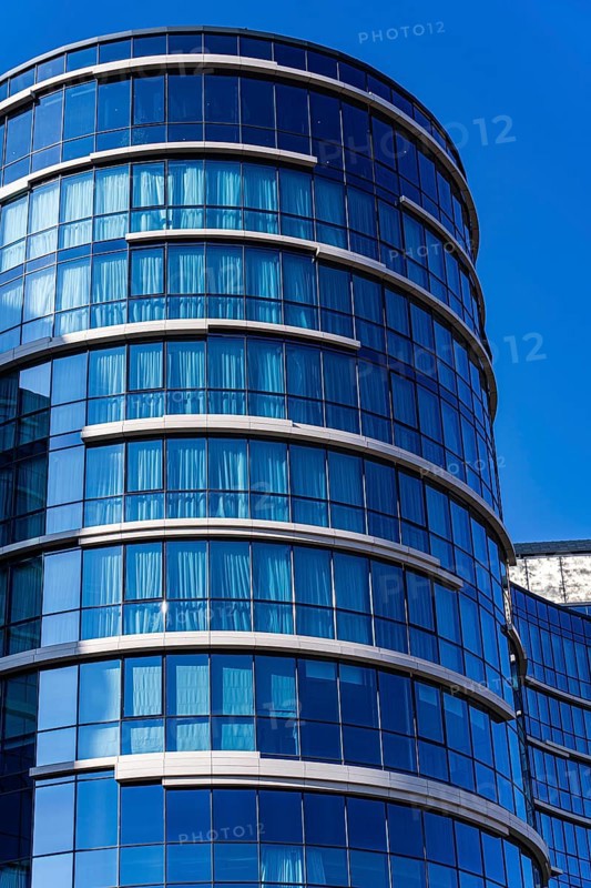 A stunning example of modern architecture featuring a curved glass facade with visible concrete and metal elements, set against a vivid blue sky