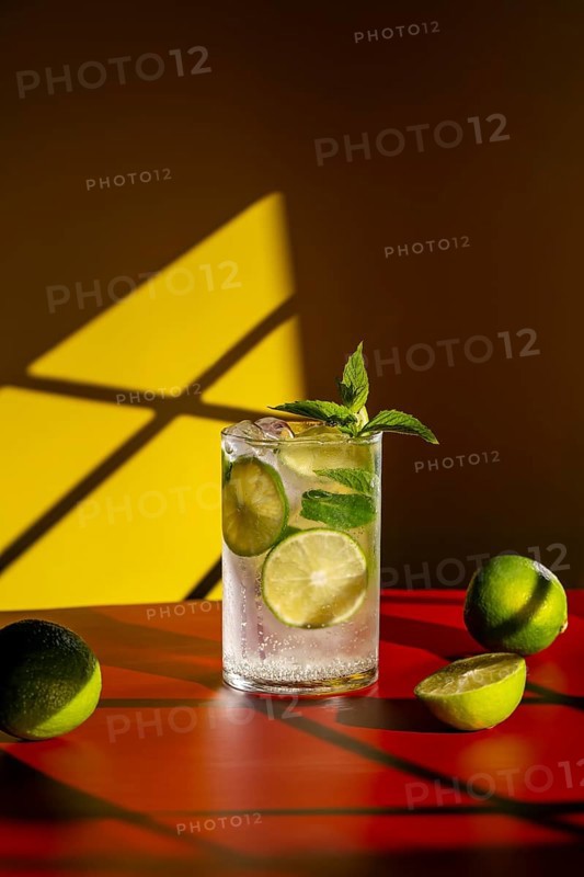 Vibrant image of a classic mojito, featuring fresh lime slices and mint leaves. Set against a bold red surface and warm yellow and brown shadows, emphasizing a lively ambiance