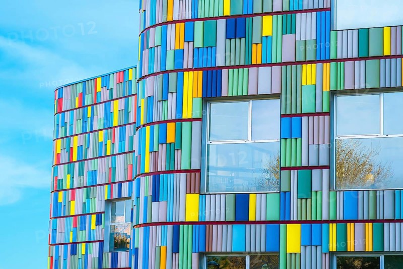 A stunning view of a modern building's curved facade adorned with multicolored panels. Bright blues, yellows, reds, and greens create a visually captivating pattern