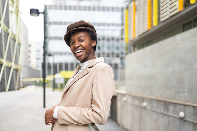 A stylish black woman smiles confidently while standing in a modern urban environment Her chic attire and joyful demeanor reflect empowerment and elegance