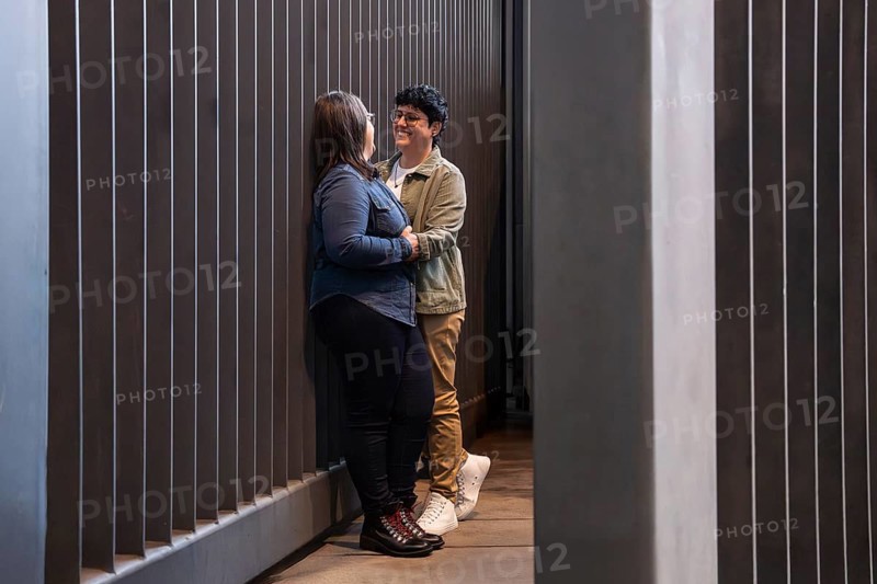 A lesbian couple shares a tender moment in an urban setting, expressing love and connection. The modern backdrop highlights their affection and vibrant interaction